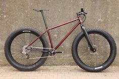 a red and black bike parked next to a wall with no wheels on the ground