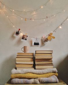 a stack of books sitting on top of a wooden table next to a string of lights