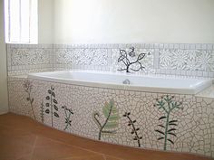 a bath tub sitting under a window next to a tiled wall with flowers on it