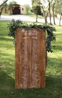 a wooden sign sitting in the grass with greenery on it's back end