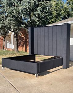 a black bed frame sitting on top of a cement floor next to a tree and building