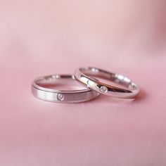 two white gold wedding rings with diamonds on pink background, close - up view from above