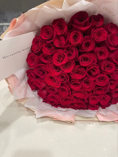 a large bouquet of red roses in a paper bag on a white tableclothed surface