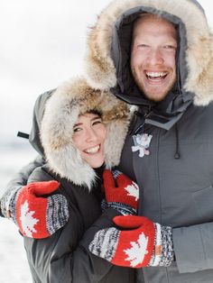 a man and woman in winter clothing standing next to each other with mittens on