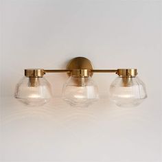 three light bathroom fixture with clear glass globes and brass finish on white wall background