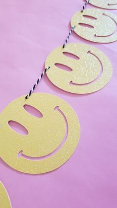 paper cut out smiley faces on a pink table with twine and black string hanging from it