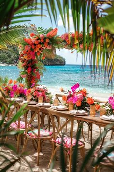 an outdoor dining area with flowers and candles on the table next to the ocean, surrounded by palm trees