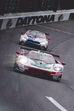 two racing cars driving on a race track with the lights on in front of them