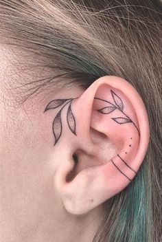 a woman's ear has a small leaf tattoo on it