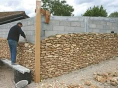 a man standing on top of a wooden bench next to a wall made out of rocks