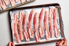 bacon strips are lined up on a baking sheet and being held by someone's hands