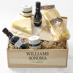 a wooden box filled with different types of cheese and condiments next to bottles of wine