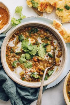 a bowl filled with beans and vegetables on top of a blue plate next to bread