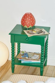 a green end table with magazines on it and a lamp next to it in the corner