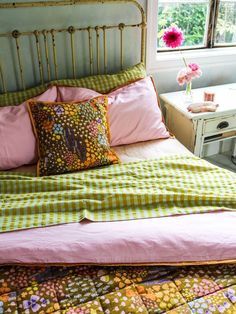 a bed with pink and green sheets in a bedroom next to a table with flowers on it