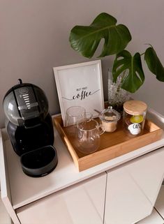 there is a coffee maker and cups on the counter next to a potted plant