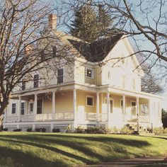 a large white house sitting on the side of a lush green field next to trees