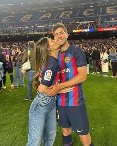 a man and woman are kissing on the field at a soccer game with fans in the stands