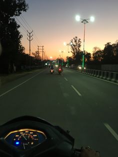 a person riding a motorcycle down a street next to traffic lights at night with the sun going down