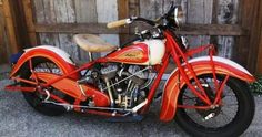 an orange and white motorcycle parked in front of a wooden fence