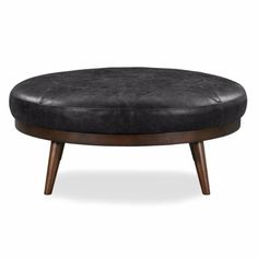 an ottoman with wooden legs and black leather upholstered cushion on the top, in front of a white background