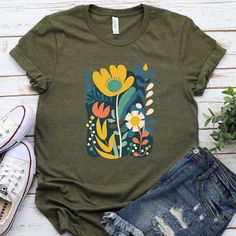 Ignite your love for the natural world with our Wildflower Whimsy T-shirt! Boasting lush wildflower designs, this floral shirt is a breath of fresh air in your wardrobe. It's more than just a tee; it's a testament to the vintage charm, adding a touch of nostalgia to your lineup of women's graphic tees. Ideal for the nature enthusiast or the one who adores a laid-back look, this wildflower shirt is sure to be a hit. Experience the alluring beauty of wildflowers every time you wear it. And don't f Relaxed Fit Green T-shirt With Plant Print, Green Graphic Tee With Plant Print, Green Graphic Tee With Plants Print, Green Cotton T-shirt With Plant Print, Casual Green Tops With Plant Print, Green T-shirt With Plants Print, Relaxed Fit, Green Relaxed Fit Shirt With Plant Print, Green Shirt With Plants Print And Relaxed Fit, Relaxed Fit T-shirt With Plants Print