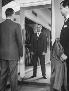 two men in suits look at their reflection in the mirror while another man looks on