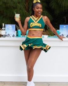 a woman in a green and yellow cheerleader outfit is holding a drink while posing for the camera