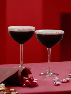 two wine glasses filled with dark liquid and candy canes on a red tablecloth