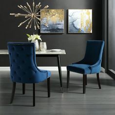 two blue chairs sitting next to each other in front of a dining room table with artwork on the wall