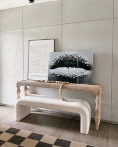 a white bench sitting next to a painting on top of a wooden table in front of a window