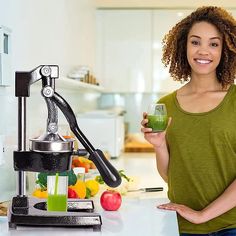 a woman holding a cup in her hand while standing next to a juicer and blender