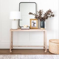 a wooden table with a mirror and vases on it next to a wicker basket