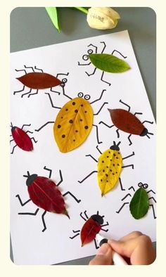 a child's hand is drawing leaves on a paper with ladybugs