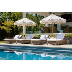 three lounge chairs with umbrellas next to a swimming pool