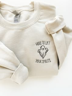 there is a white sweatshirt with a ghost embroidered on the front and an inscription that says here to lift your spirits