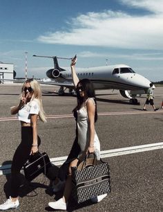 two beautiful women walking across an airport tarmac with luggage in hand and a plane behind them