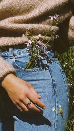 a woman with her hand on the back of her jean pants and holding flowers in her pocket