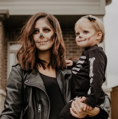 a woman holding a small child wearing skeleton makeup