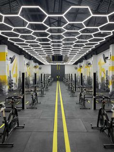 an indoor gym with yellow and white lines running through the floor, exercise bikes lined up on each side