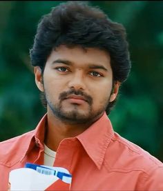 a close up of a person wearing a red shirt and looking at the camera with a serious look on his face