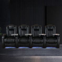 a row of black leather reclining chairs sitting next to each other in front of a wall