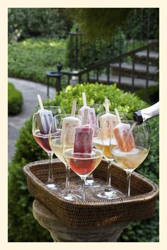 a person pours wine into several glasses on a tray in front of some bushes