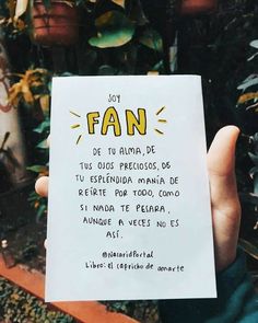 a person holding up a piece of paper with writing on it in front of some plants