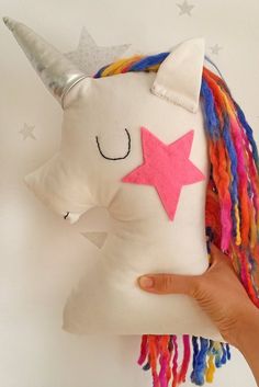 a hand holding a white stuffed unicorn with multi - colored dreadlocks and a pink star