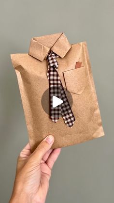 a hand holding a brown paper bag with a tie on it and a button up shirt