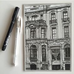 a black and white drawing of a building next to a ballpoint pen on a table