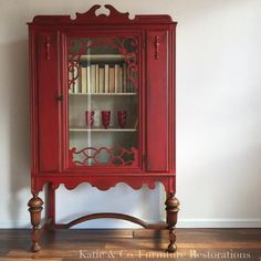 a red china cabinet with glass doors on the top and bottom shelves, in front of a white wall