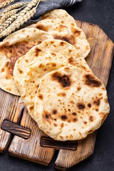 three flat breads on a cutting board next to some ears of wheat and a knife