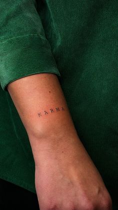 a woman's arm with the word karma tattooed on her left wrist, in cursive font